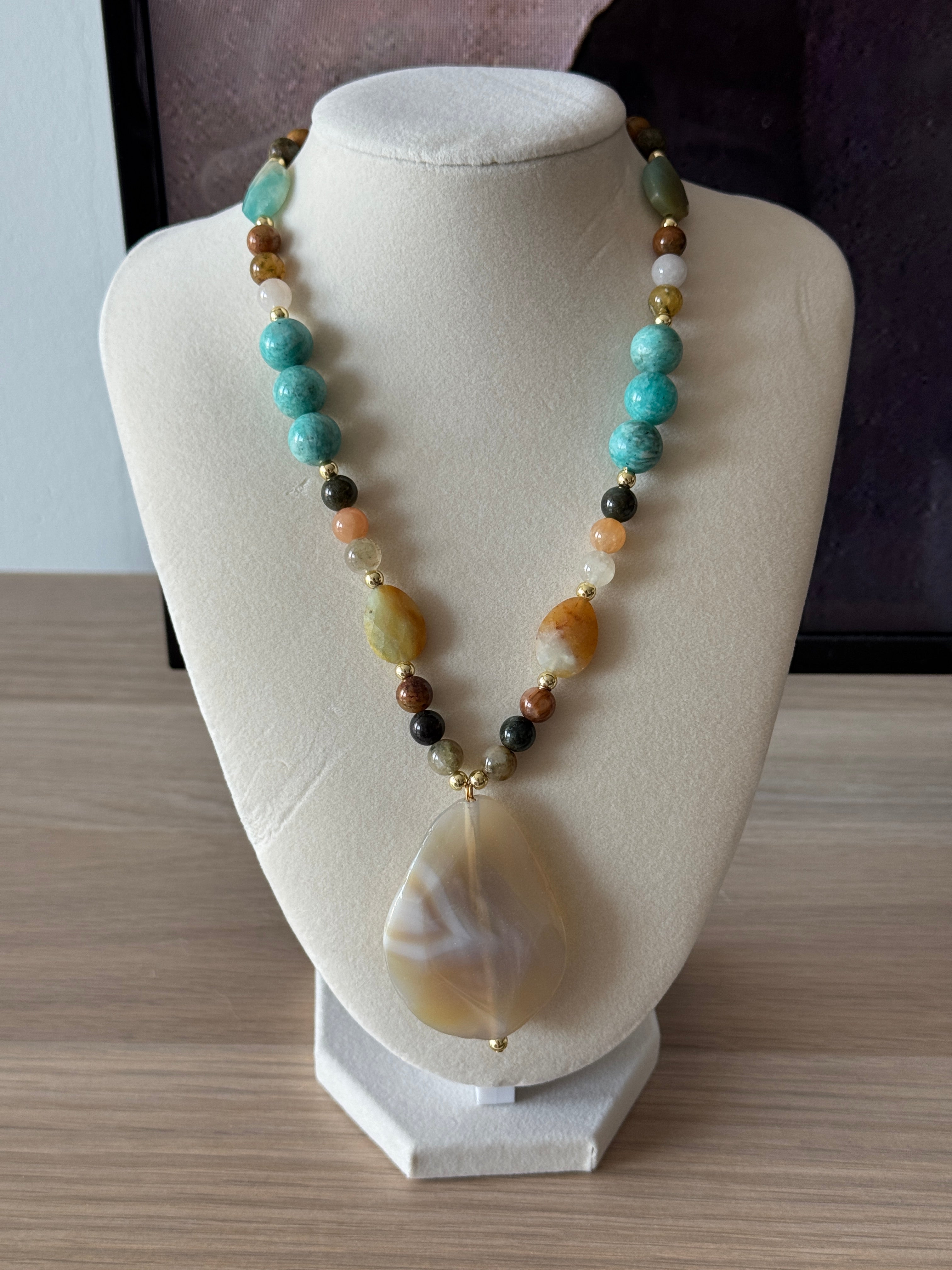 Necklace with multicolored beads on a white stand against a neutral background