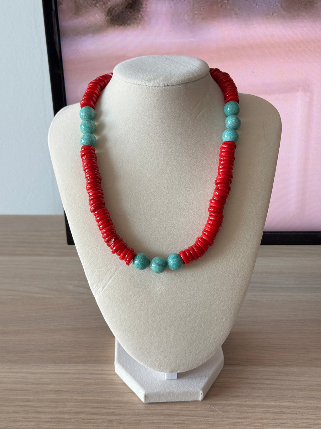 Necklace with red and turquoise beads on a white hat against a light pink background