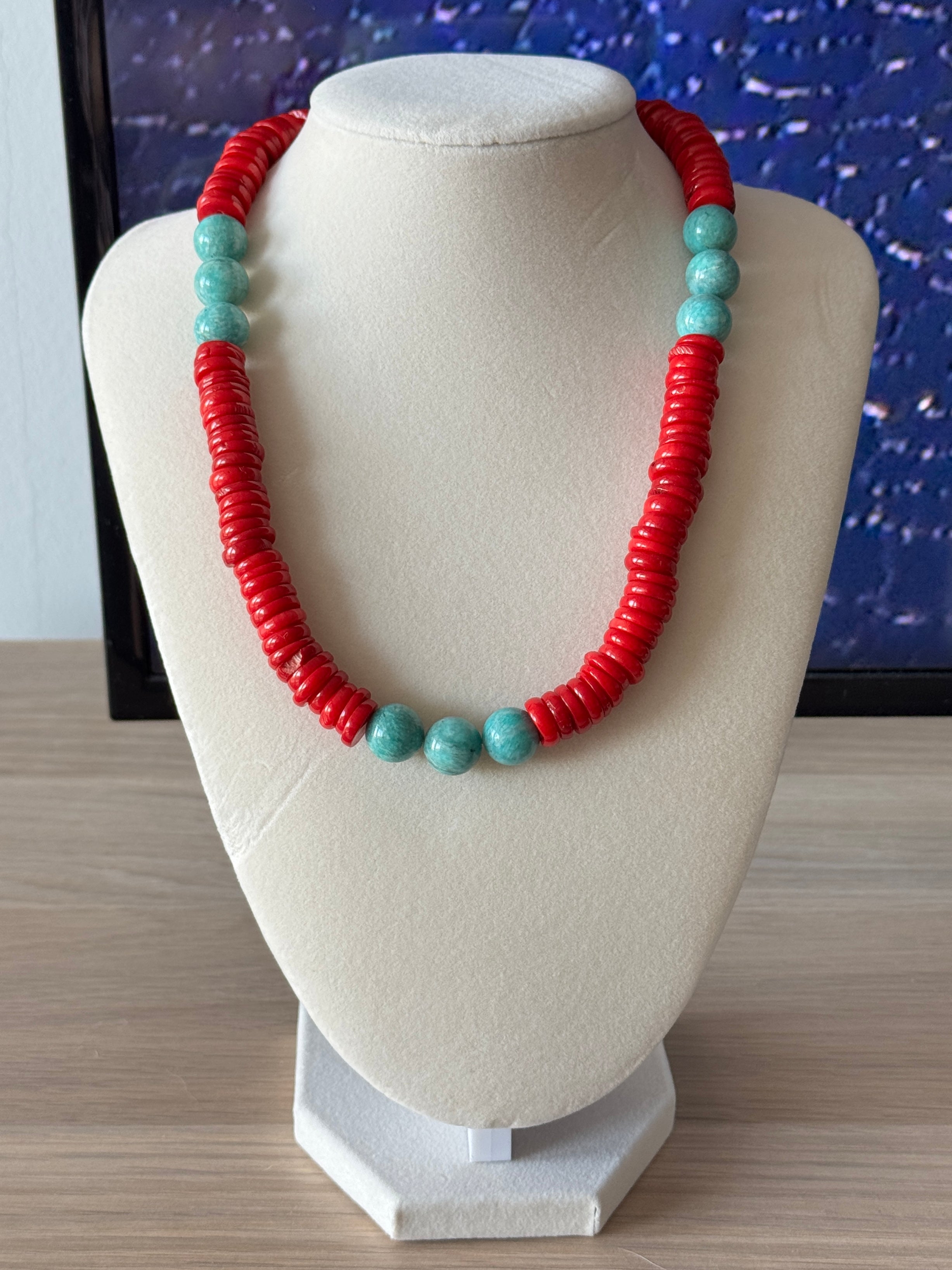 Necklace with red and turquoise beads on a white bust against a blue textured background