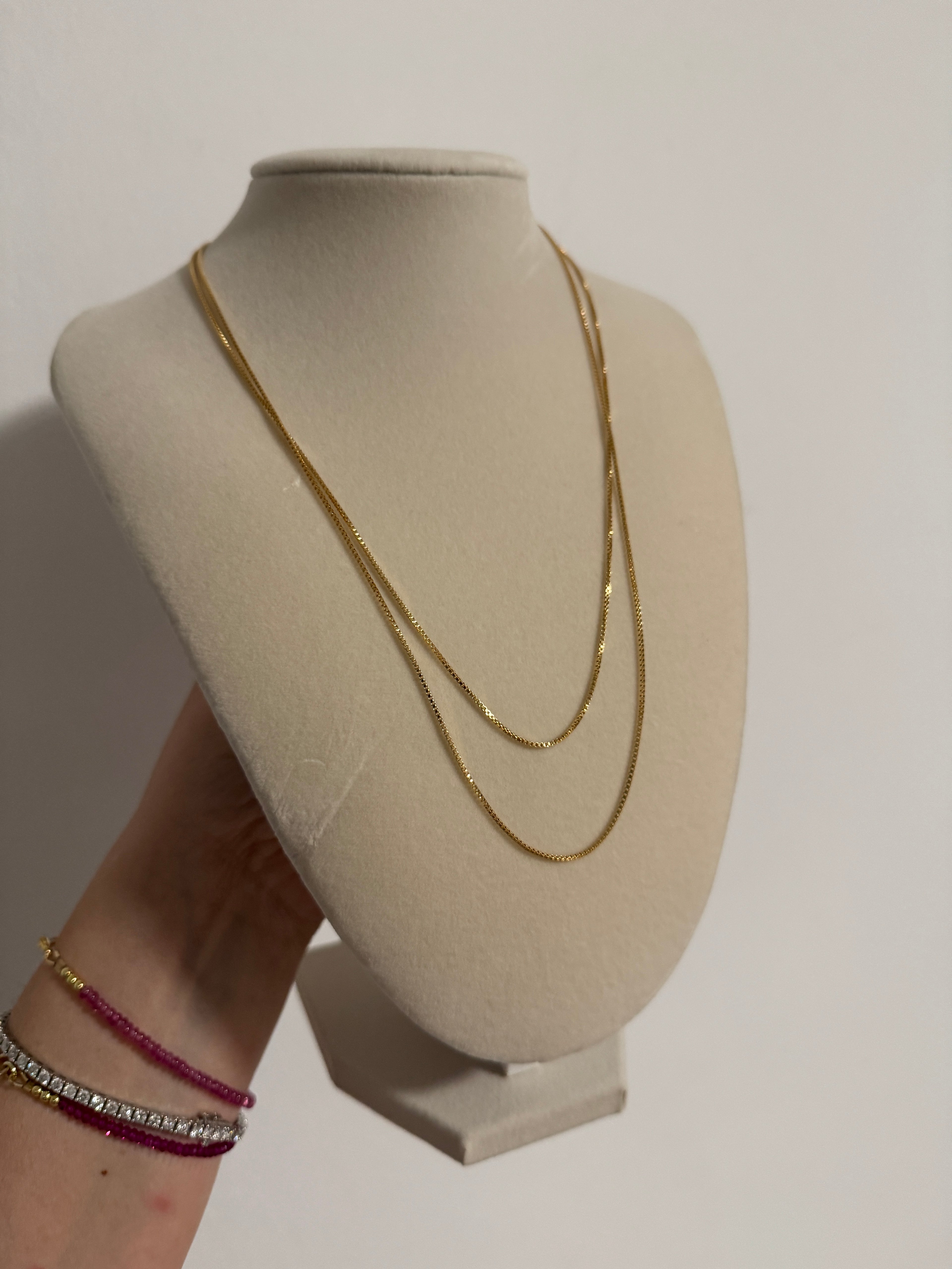 Gold necklace on a beige jewelry display with a plain background